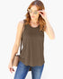 A woman wearing a sleeveless olive brown tank top, blue jeans, and sunglasses, carrying a beige crossbody bag against a plain white background.