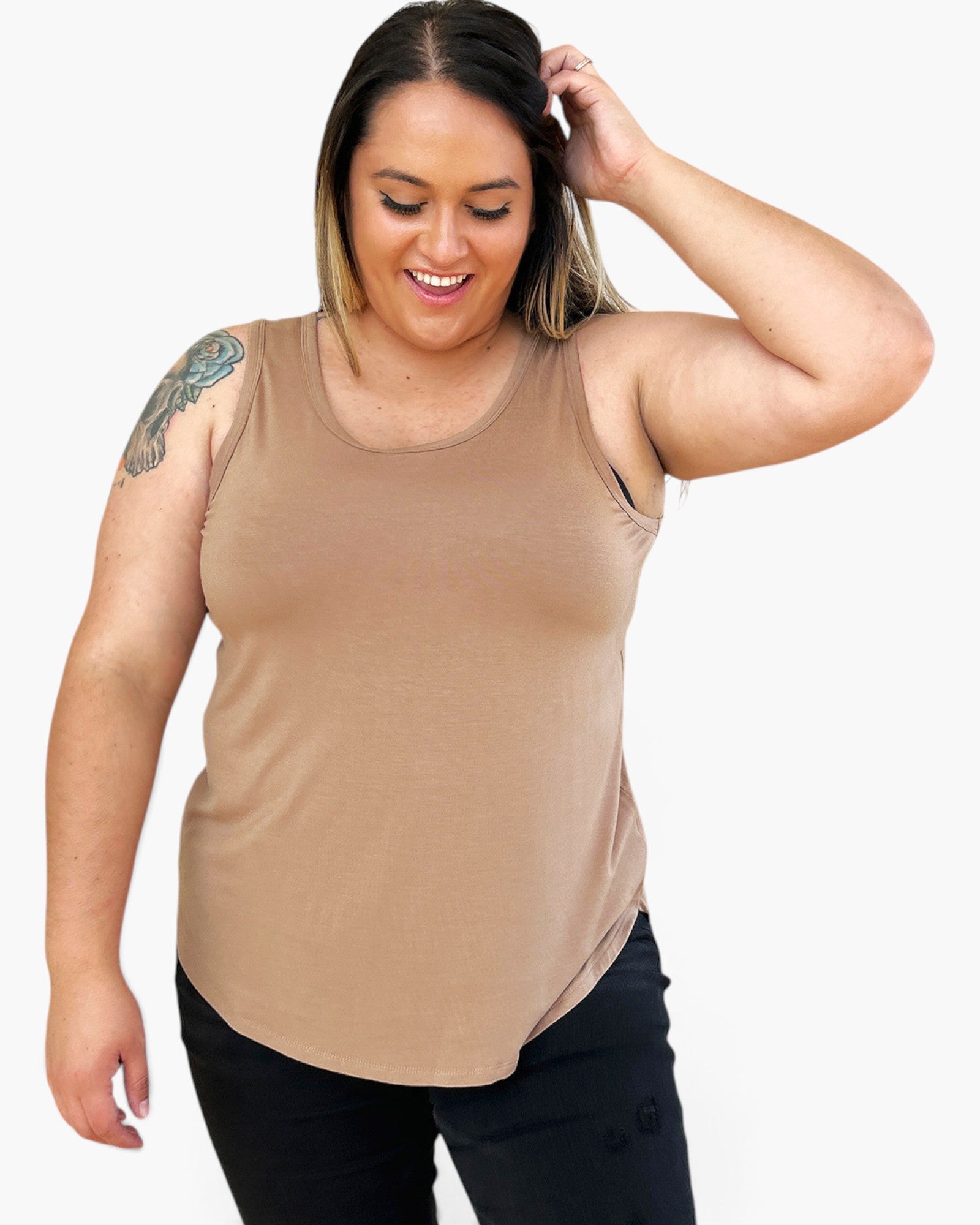 A woman modeling a scoop-neck, sleeveless tank top in a light tan color, paired with black pants, against a plain white background.