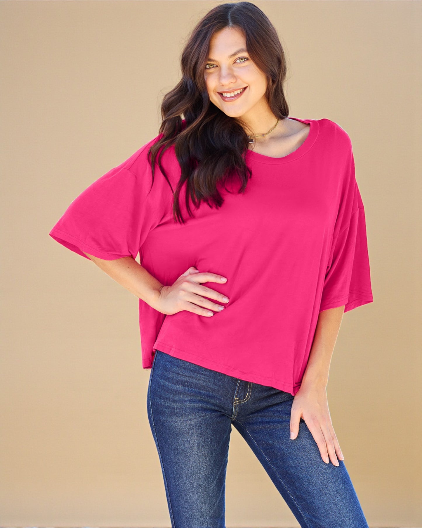 Woman wearing a bright pink top and blue jeans on a beige background