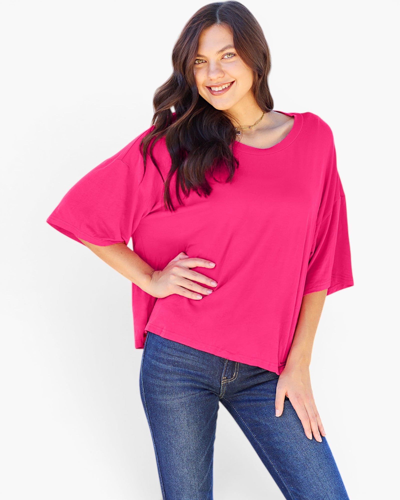 A woman modeling a bright pink short-sleeve top with a relaxed, oversized fit and blue jeans against a plain white background.