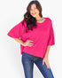A woman modeling a bright pink short-sleeve top with a relaxed, oversized fit and blue jeans against a plain white background.