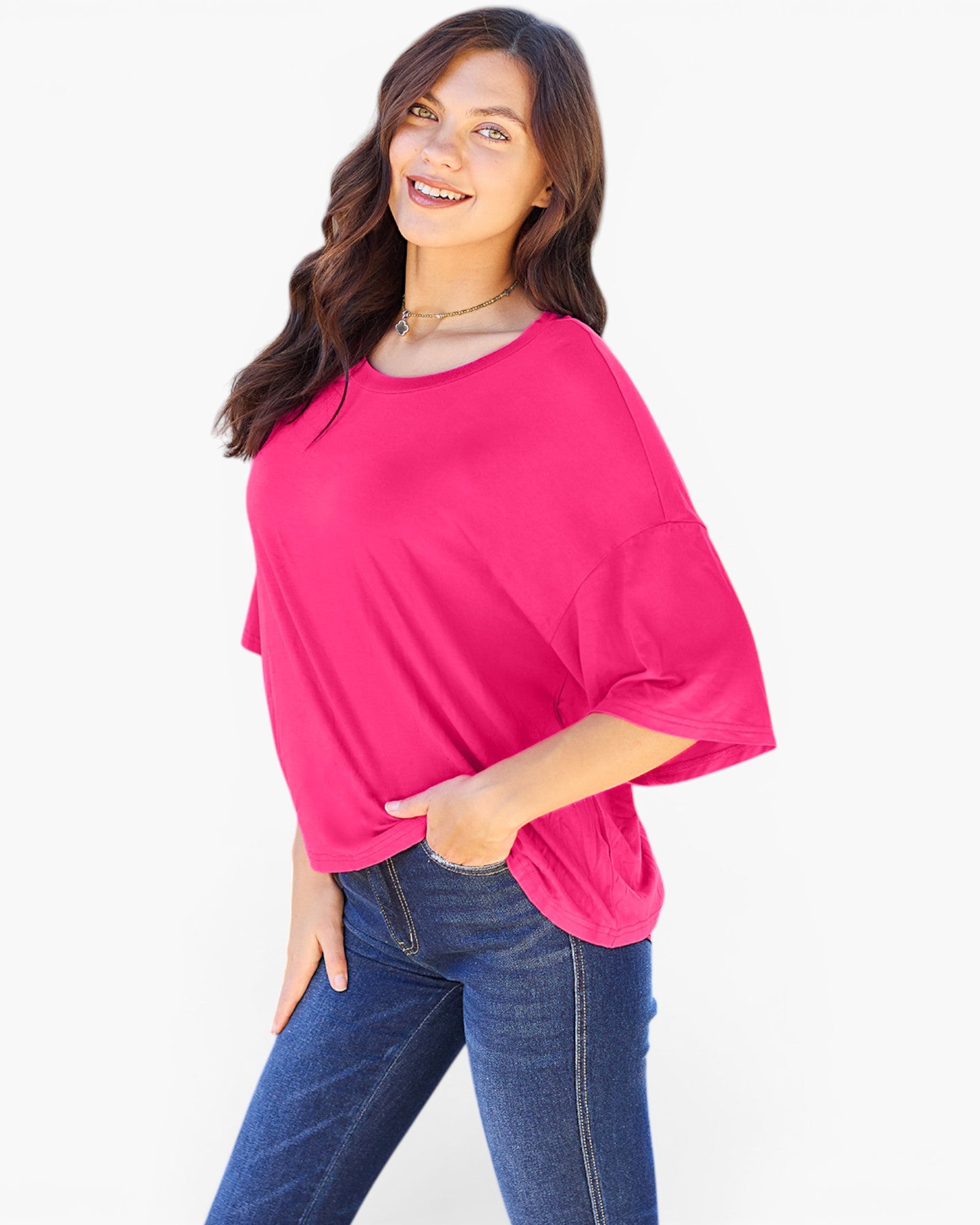 A woman wearing a bright pink short-sleeve top with elbow-length flared sleeves and blue jeans, posing against a clean white background.