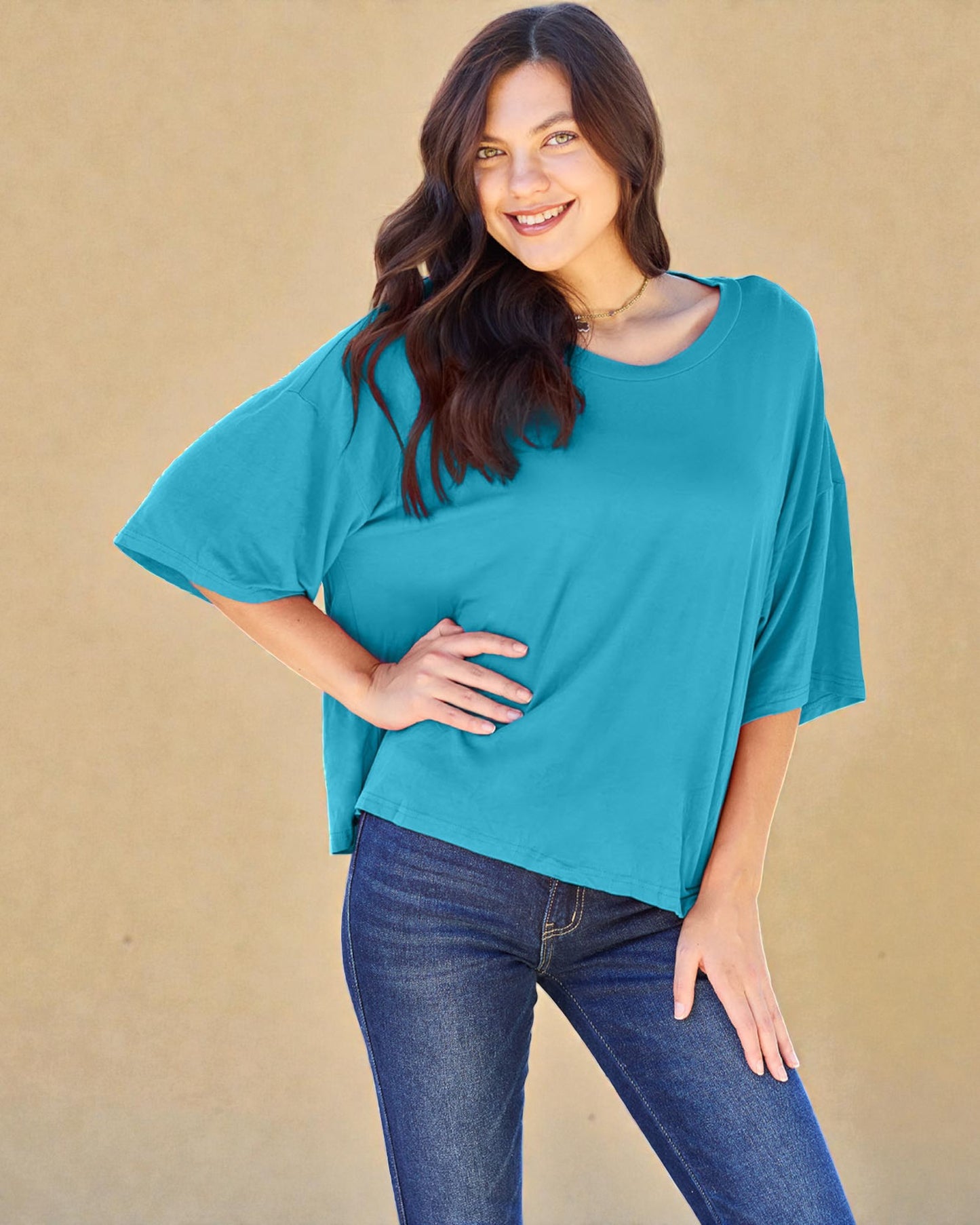 Woman wearing a teal oversized shirt and blue jeans against a beige background