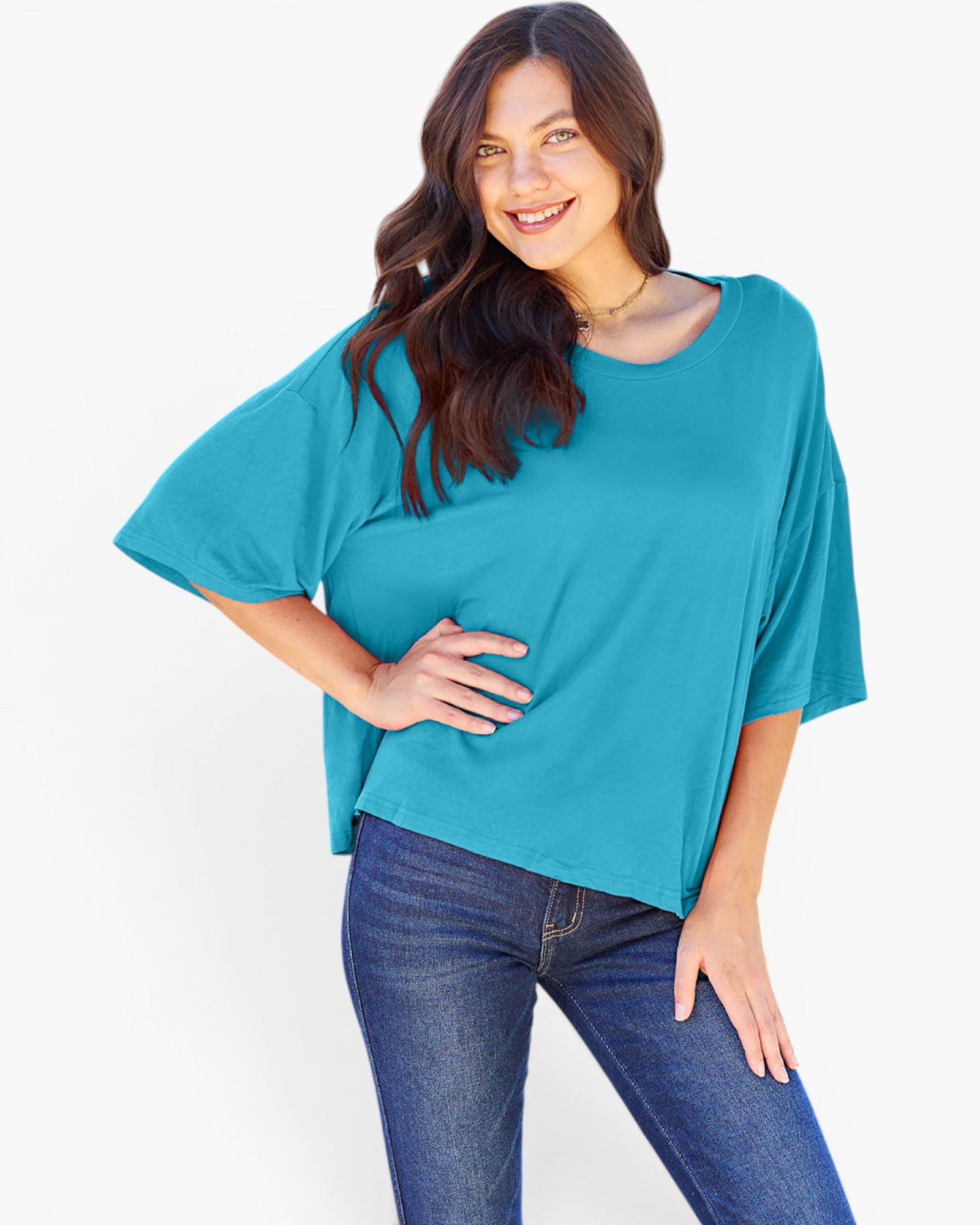 A woman wearing a teal short-sleeve top and dark blue jeans, posing against a clean white background.