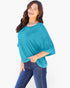 A woman modeling a teal blue short-sleeve top with a relaxed, oversized fit and side pockets, paired with dark blue jeans, against a plain white background.