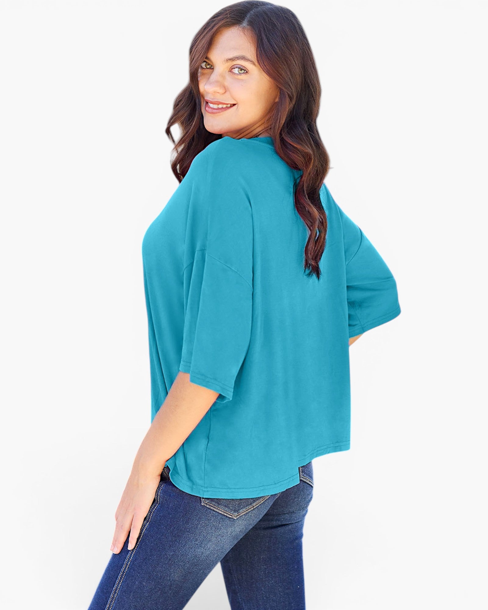 A woman wearing a teal short-sleeve top and blue jeans, photographed from the back against a plain white studio background.
