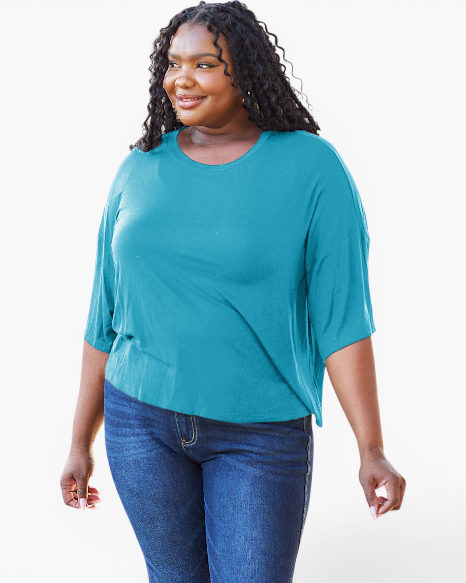 A woman modeling a teal short-sleeve top with a relaxed, draped fit and blue jeans against a plain white studio background.