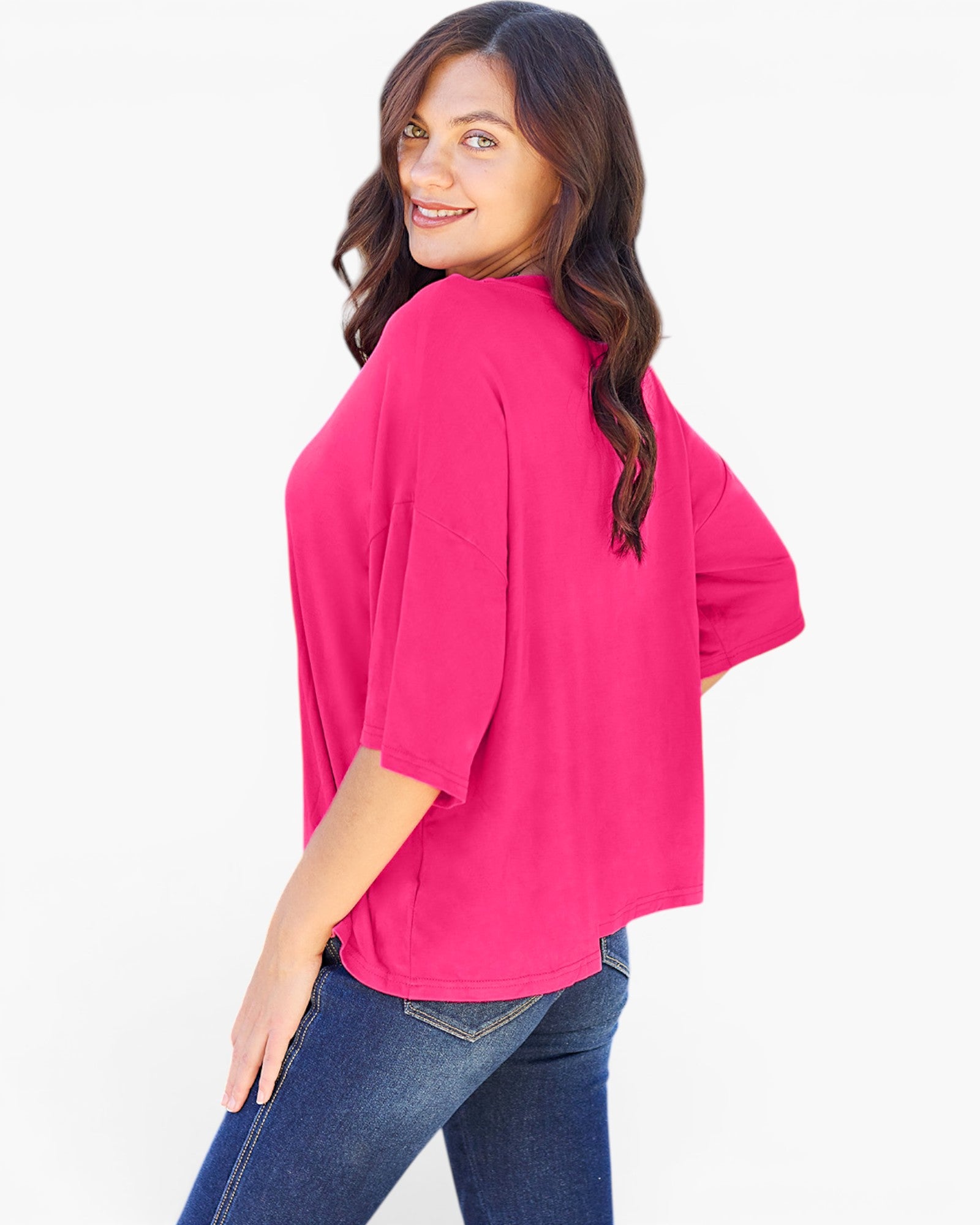 A woman wearing a bright pink short-sleeve top and blue jeans, photographed from the back against a plain white studio background.