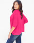 A woman wearing a bright pink short-sleeve top and blue jeans, photographed from the back against a plain white studio background.