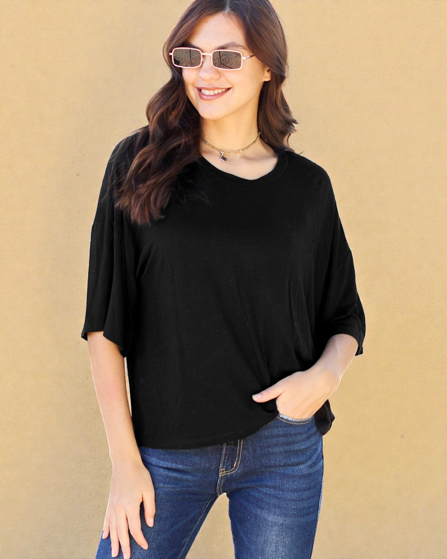 Woman wearing a black top and blue jeans against a beige background