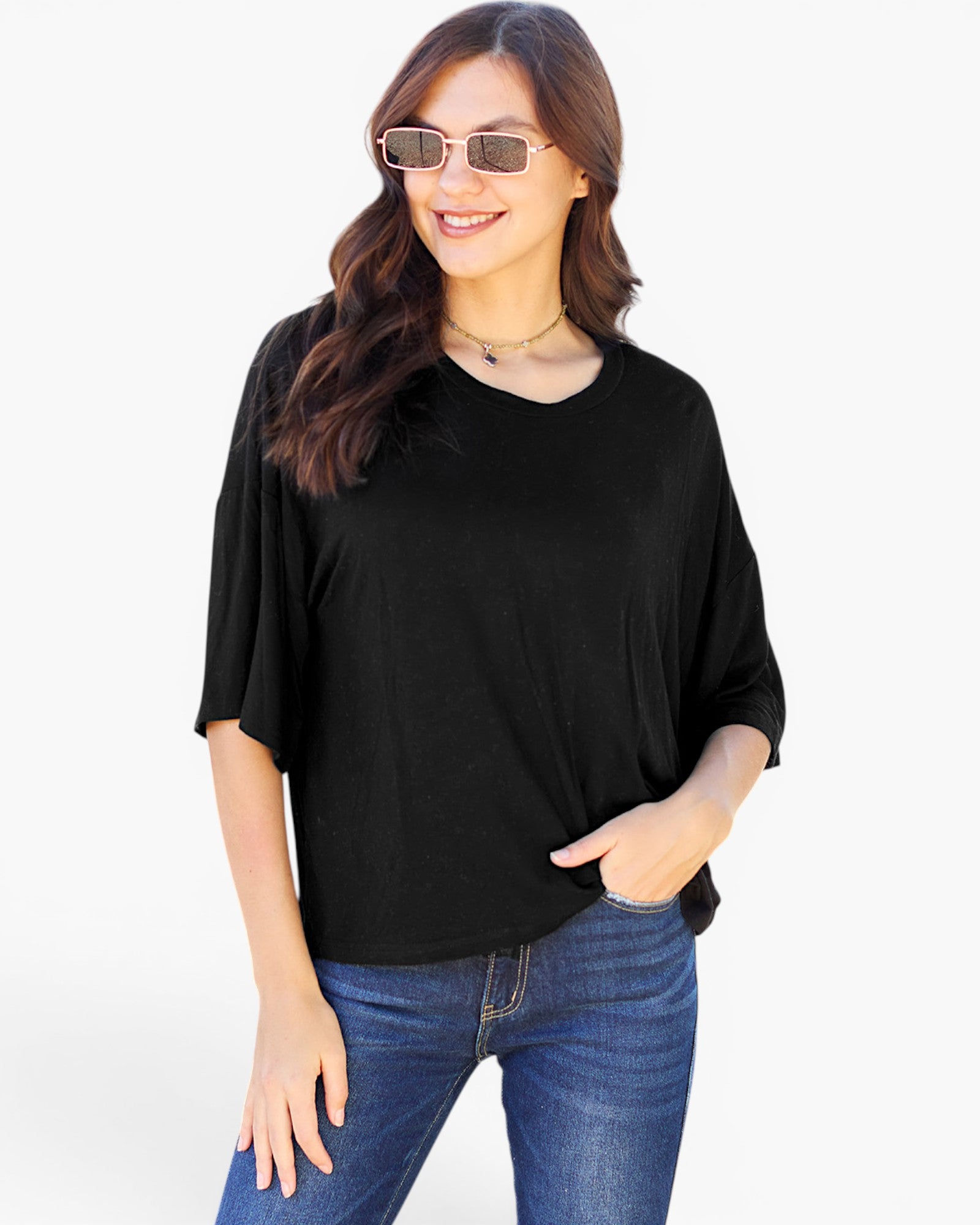 A woman wearing a black short-sleeve V-neck top and blue jeans, standing against a plain white studio background.