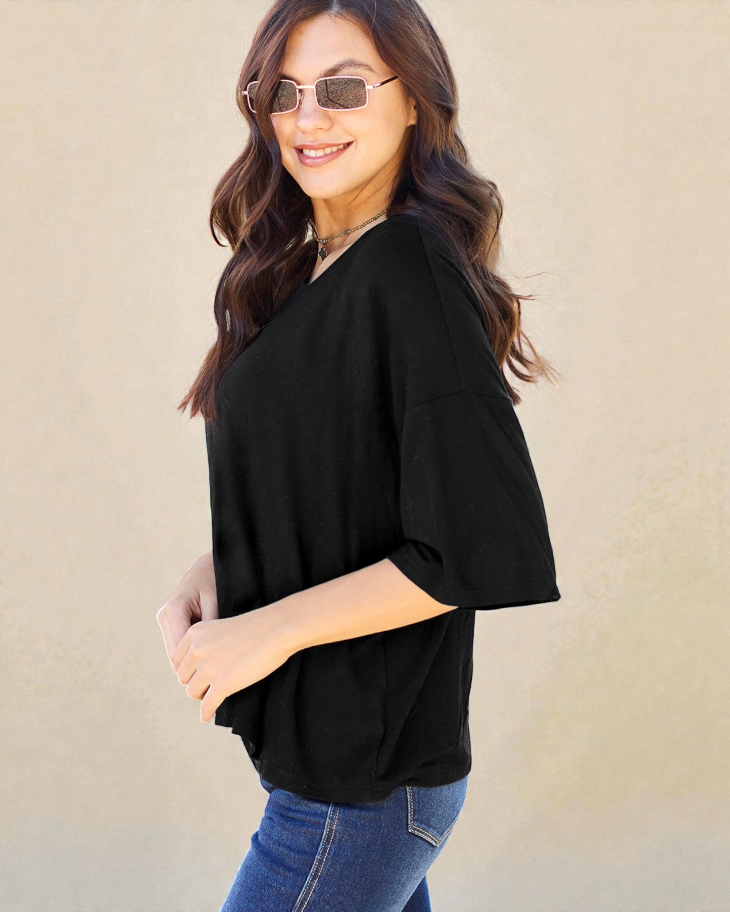 Woman wearing a black top and sunglasses against a beige background