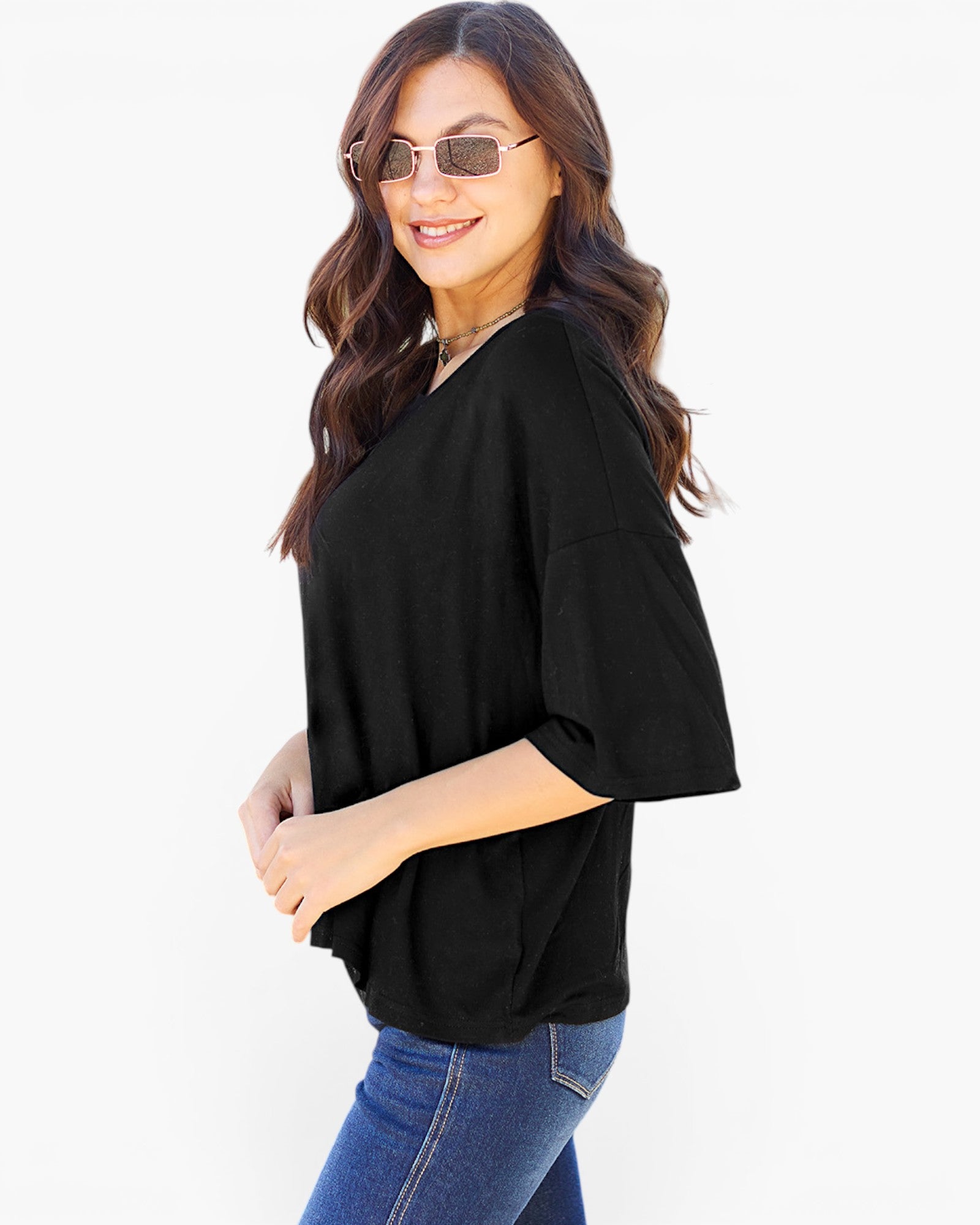 A woman modeling a black short-sleeve V-neck top with a relaxed, oversized fit, paired with blue jeans against a plain white background.