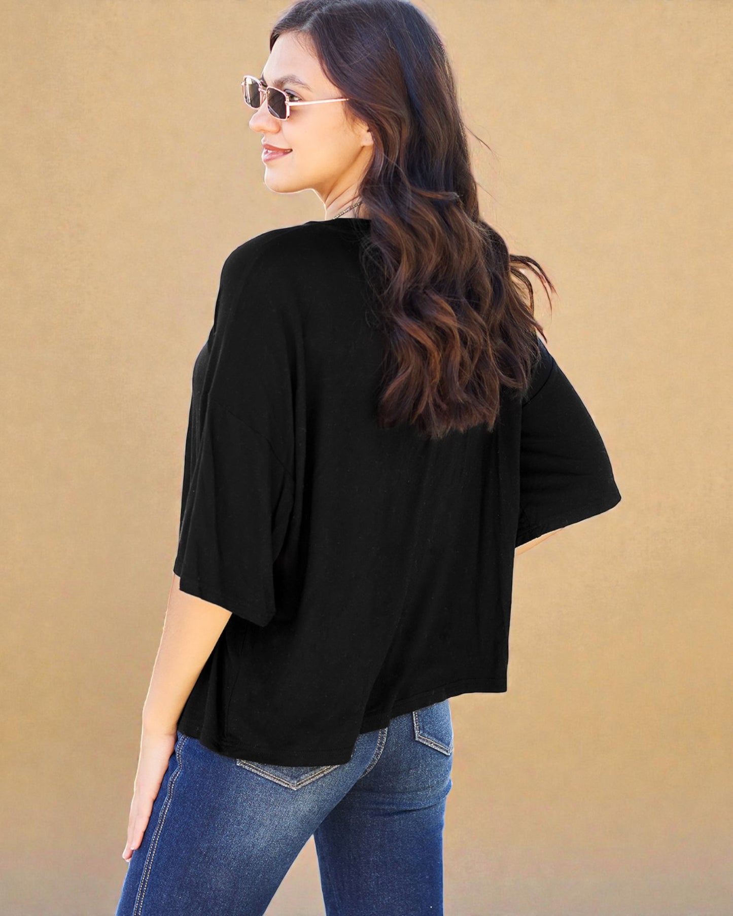 Woman wearing a black top and blue jeans against a beige background