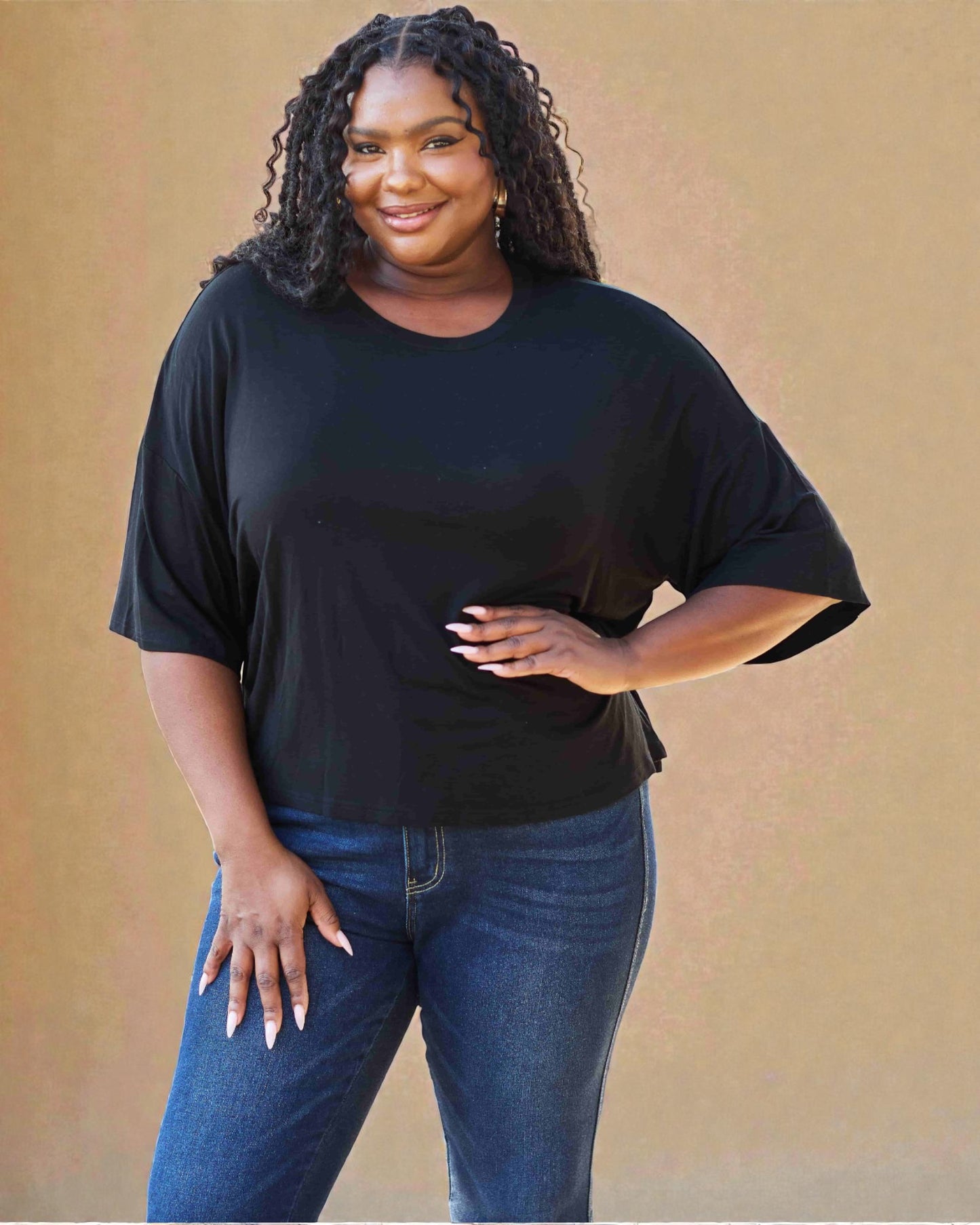 Woman wearing a black t-shirt and blue jeans against a beige background