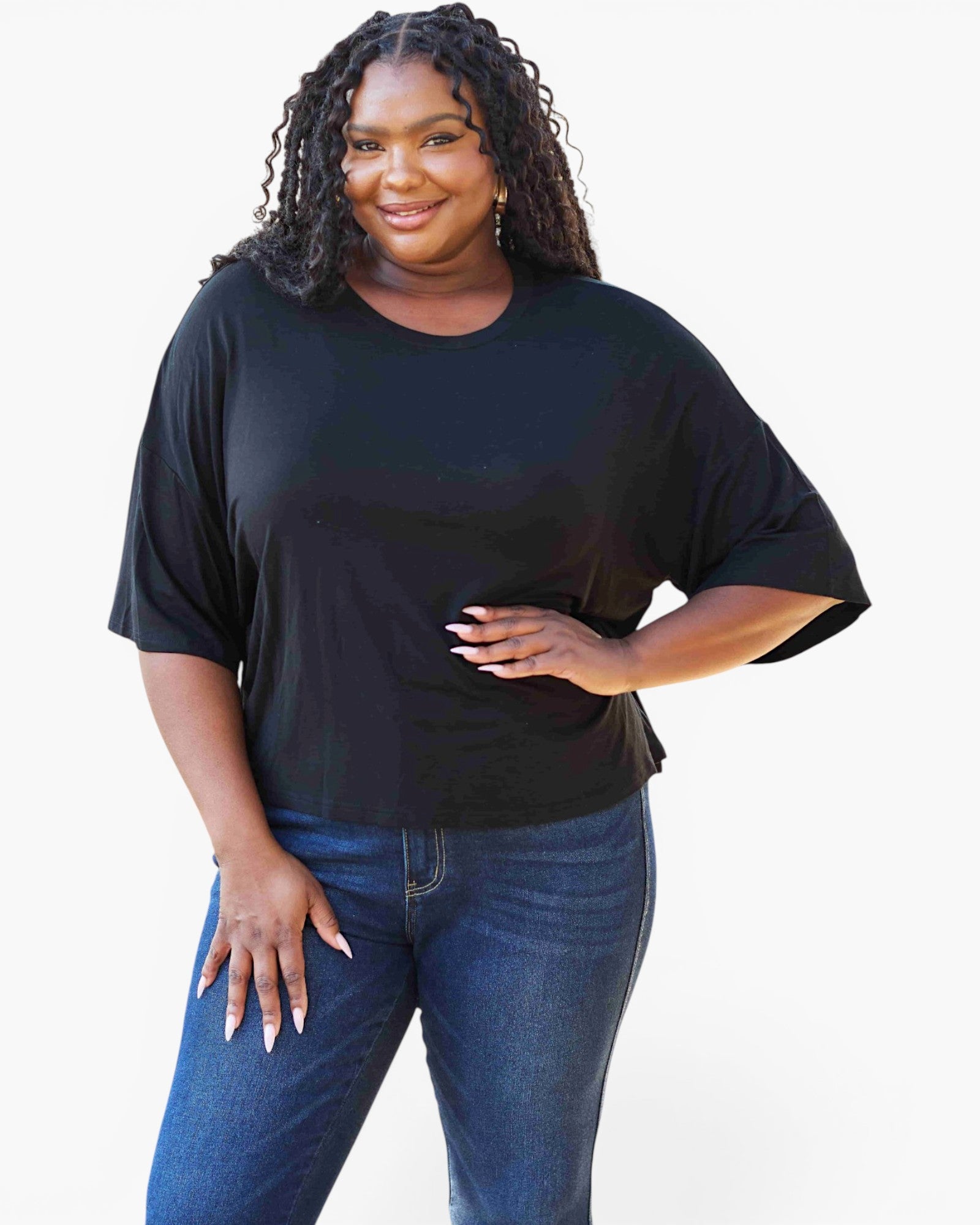 A woman modeling a black short-sleeve t-shirt with a relaxed, oversized fit, paired with blue jeans, against a plain white background.