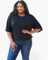 A woman modeling a black short-sleeve t-shirt with a relaxed, oversized fit, paired with blue jeans, against a plain white background.