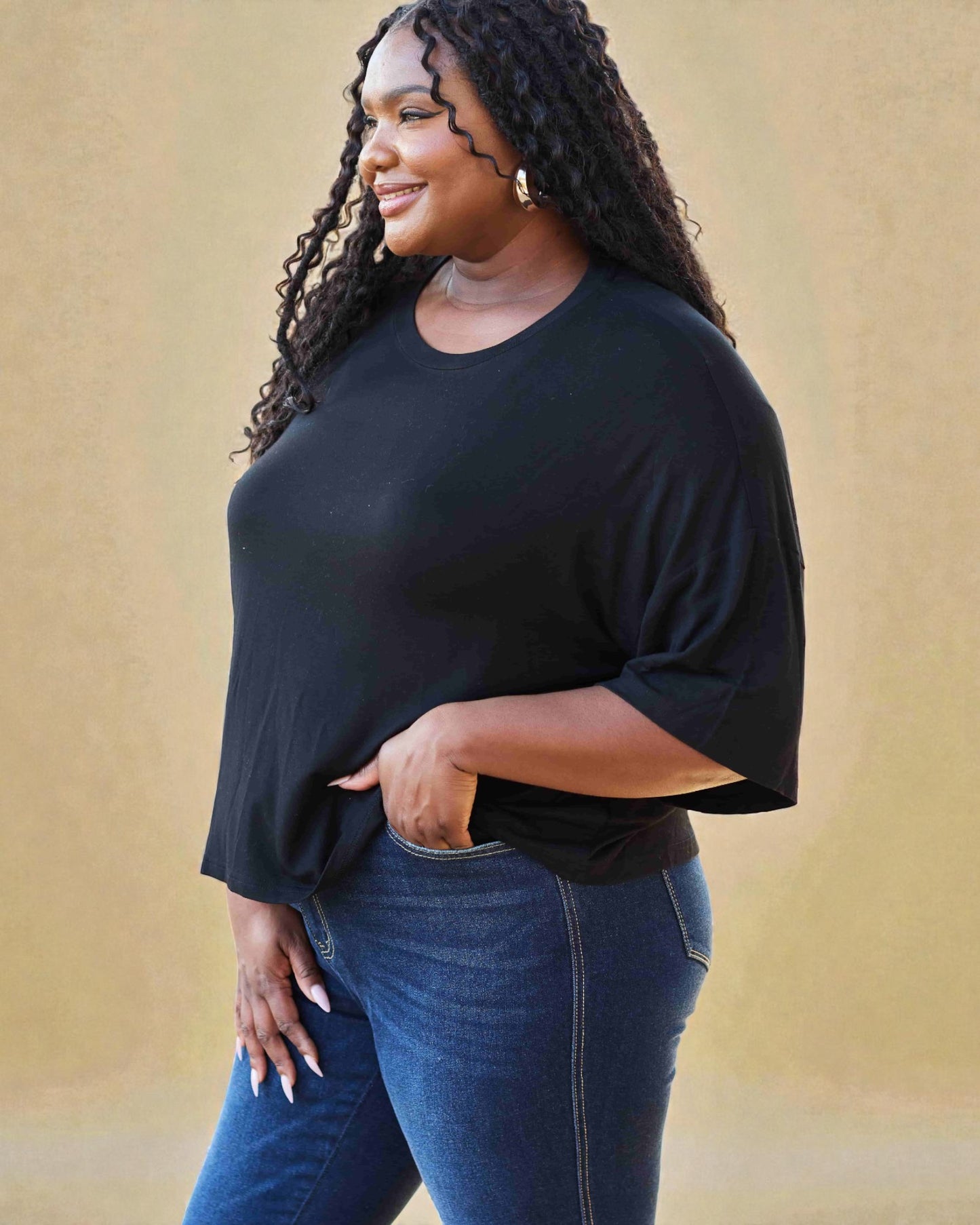 Woman wearing a black top and blue jeans against a beige background