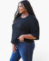 A woman modeling a black short-sleeve crewneck top with a relaxed, slightly oversized fit, paired with dark blue jeans against a plain white background.