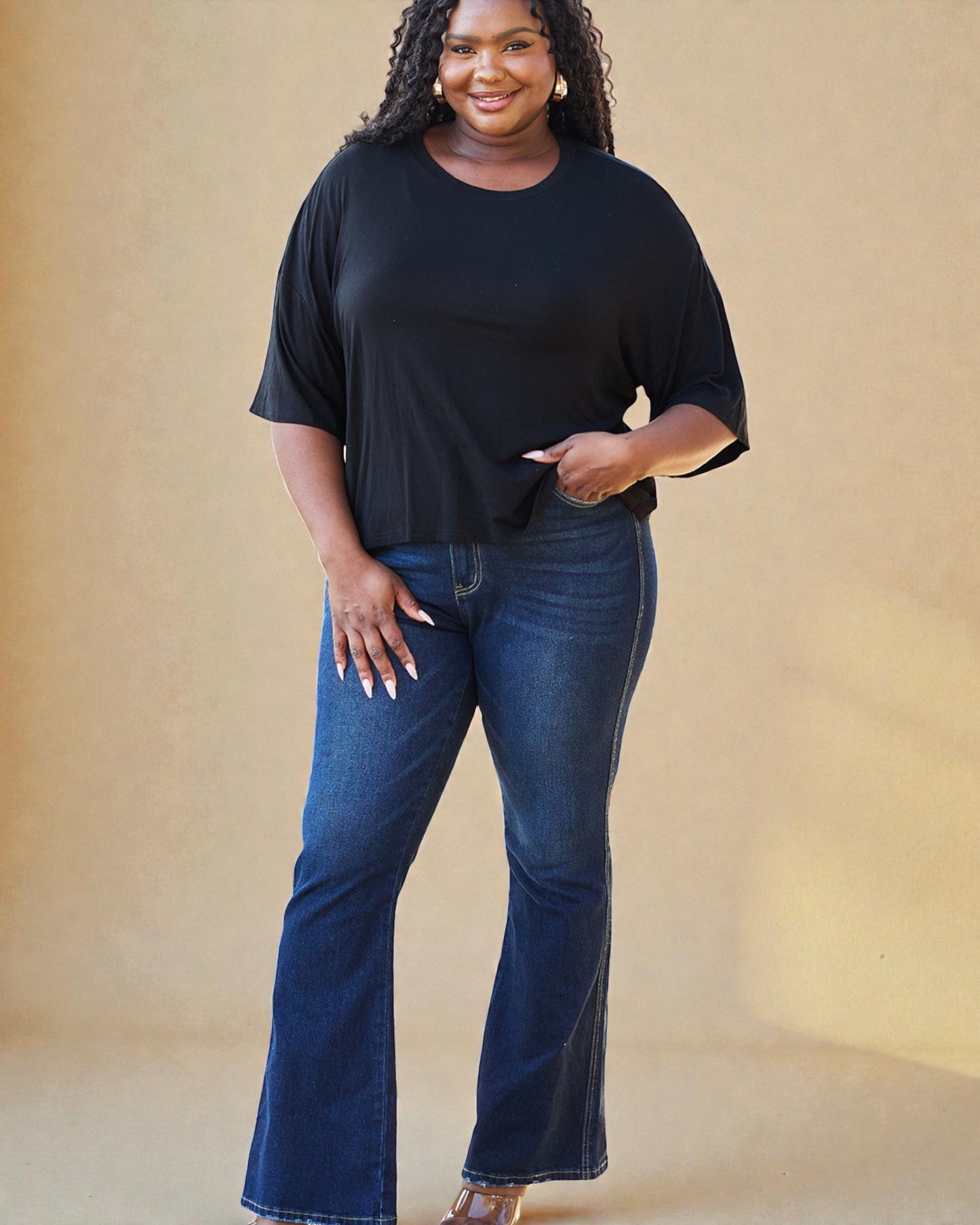 Woman wearing a black top and blue jeans against a beige background