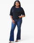 A woman modeling a black short-sleeve crewneck top and dark blue flare jeans against a plain white studio background.