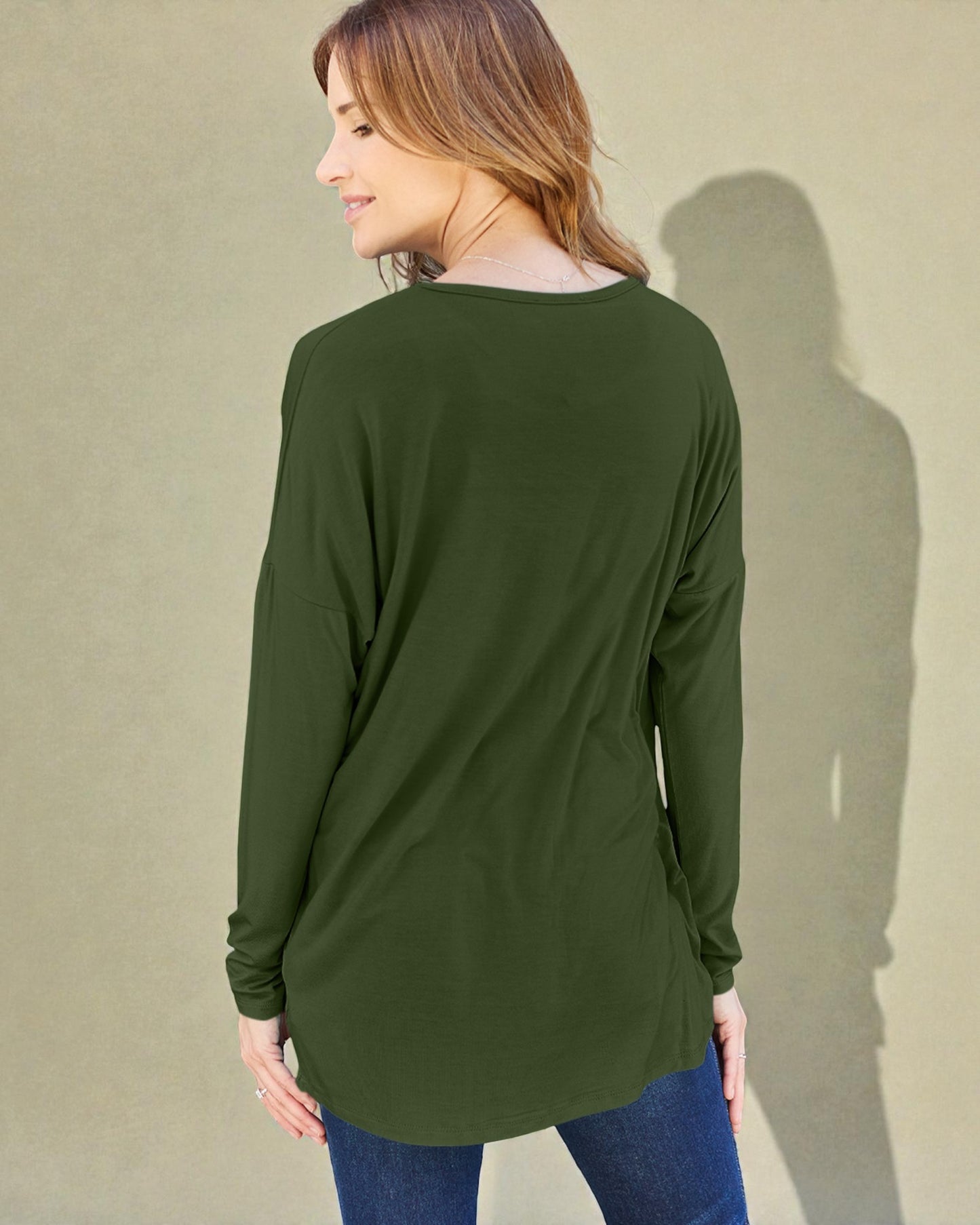 Woman wearing a green long-sleeve top against a beige wall