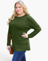A woman modeling a long-sleeve crewneck top in olive green, paired with blue jeans and holding a brown shoulder bag, against a plain light gray background.