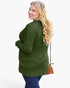 A woman with long blonde hair is shown from the back wearing an olive green long-sleeve tunic top and blue jeans, holding a brown crossbody purse against a plain white background.