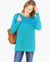 A woman wearing a bright turquoise long-sleeve tunic top and blue jeans, carrying a brown woven shoulder bag against a plain white background.