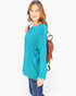 A woman modeling a teal long-sleeve crewneck top, paired with blue jeans and a brown woven backpack, against a plain white studio background.