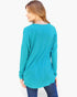 A woman wearing a teal long-sleeve tunic top and blue jeans, shown from a back-three-quarter view against a plain white studio background.