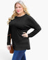 A woman modeling a black long-sleeve crewneck top with a relaxed fit, paired with blue jeans, against a plain white background.