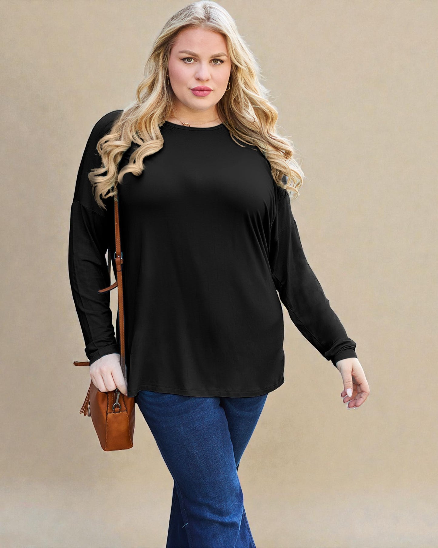 Woman wearing a black long-sleeve top and blue jeans against a beige background