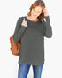A woman wearing a dark gray long-sleeve tunic top and blue jeans, carrying a brown woven shoulder bag against a plain white background.