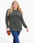 A woman modeling a dark olive green long-sleeve top with blue jeans, holding a brown leather crossbody bag against a plain white background.