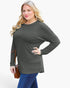 A woman modeling a dark olive green long-sleeve top with a relaxed fit, paired with blue jeans, against a plain white background.