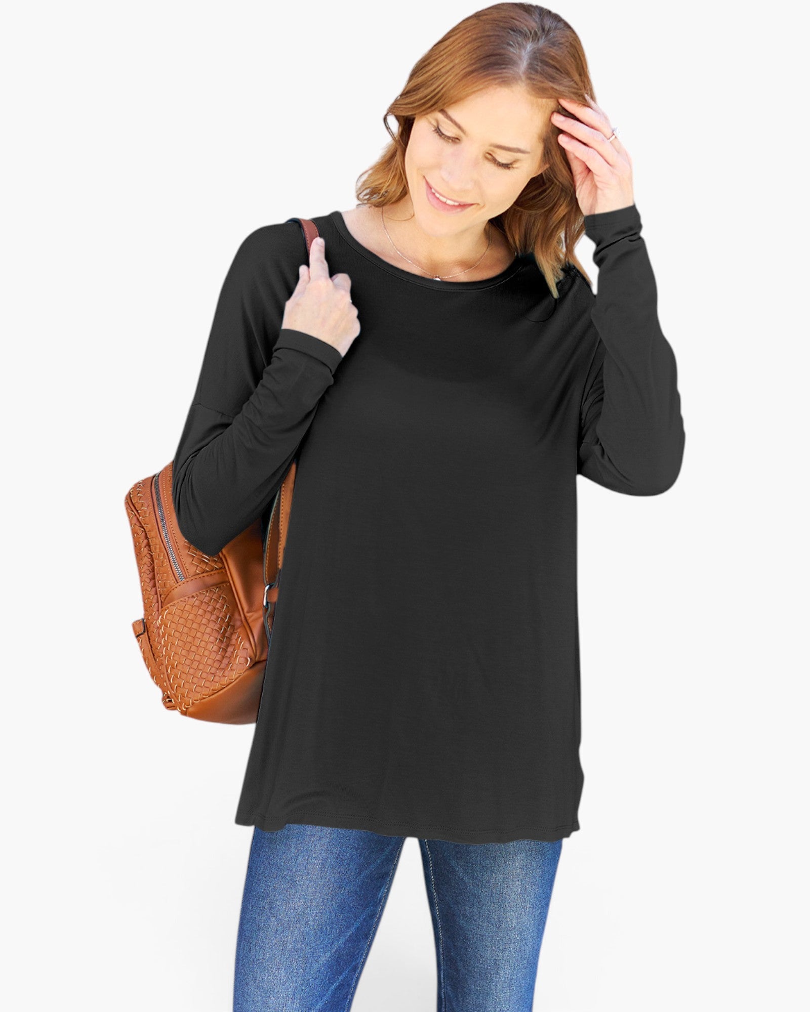A woman wearing a black long-sleeve tunic top and blue jeans, carrying a brown woven shoulder bag against a plain white background.