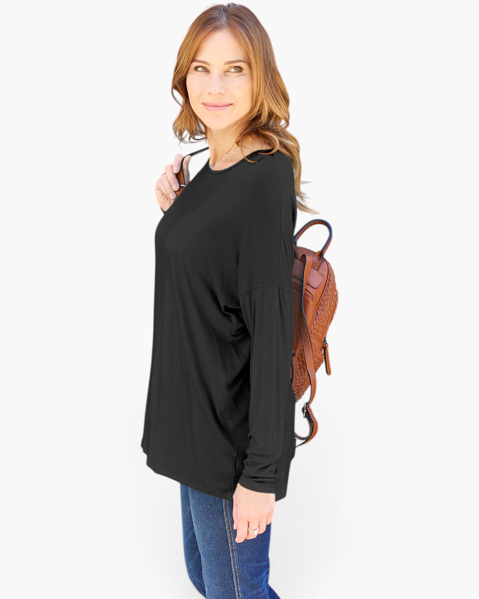 A woman modeling a black long-sleeve top with a relaxed fit, paired with blue jeans and a brown backpack, against a plain white background.