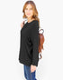 A woman modeling a black long-sleeve top with a relaxed fit, paired with blue jeans and a brown backpack, against a plain white background.