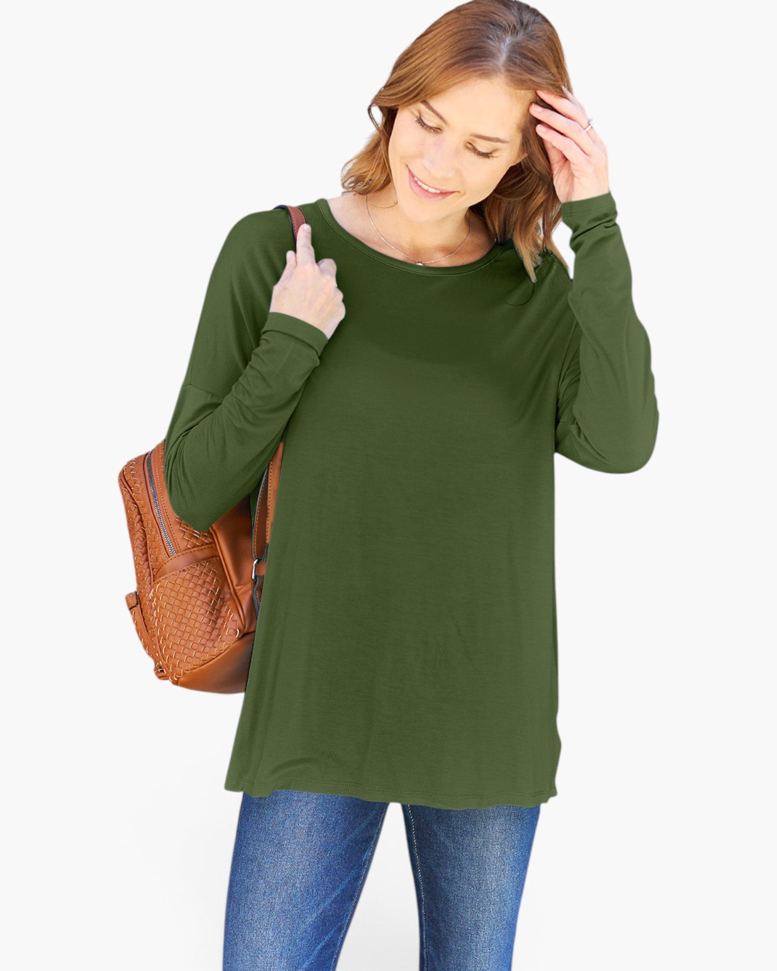 A woman wearing a long-sleeve olive green tunic top and blue jeans, carrying a brown woven shoulder bag against a plain white background.
