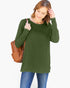 A woman wearing a long-sleeve olive green tunic top and blue jeans, carrying a brown woven shoulder bag against a plain white background.