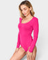 Woman wearing a bright pink long-sleeve bodysuit on a light gray background