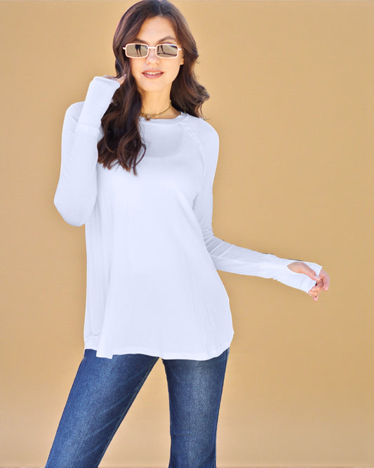 Woman wearing a white long-sleeve top and blue jeans against a beige background