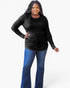 A woman modeling a black long-sleeve top with a layered scoop neck design, paired with blue jeans, against a plain white studio background.
