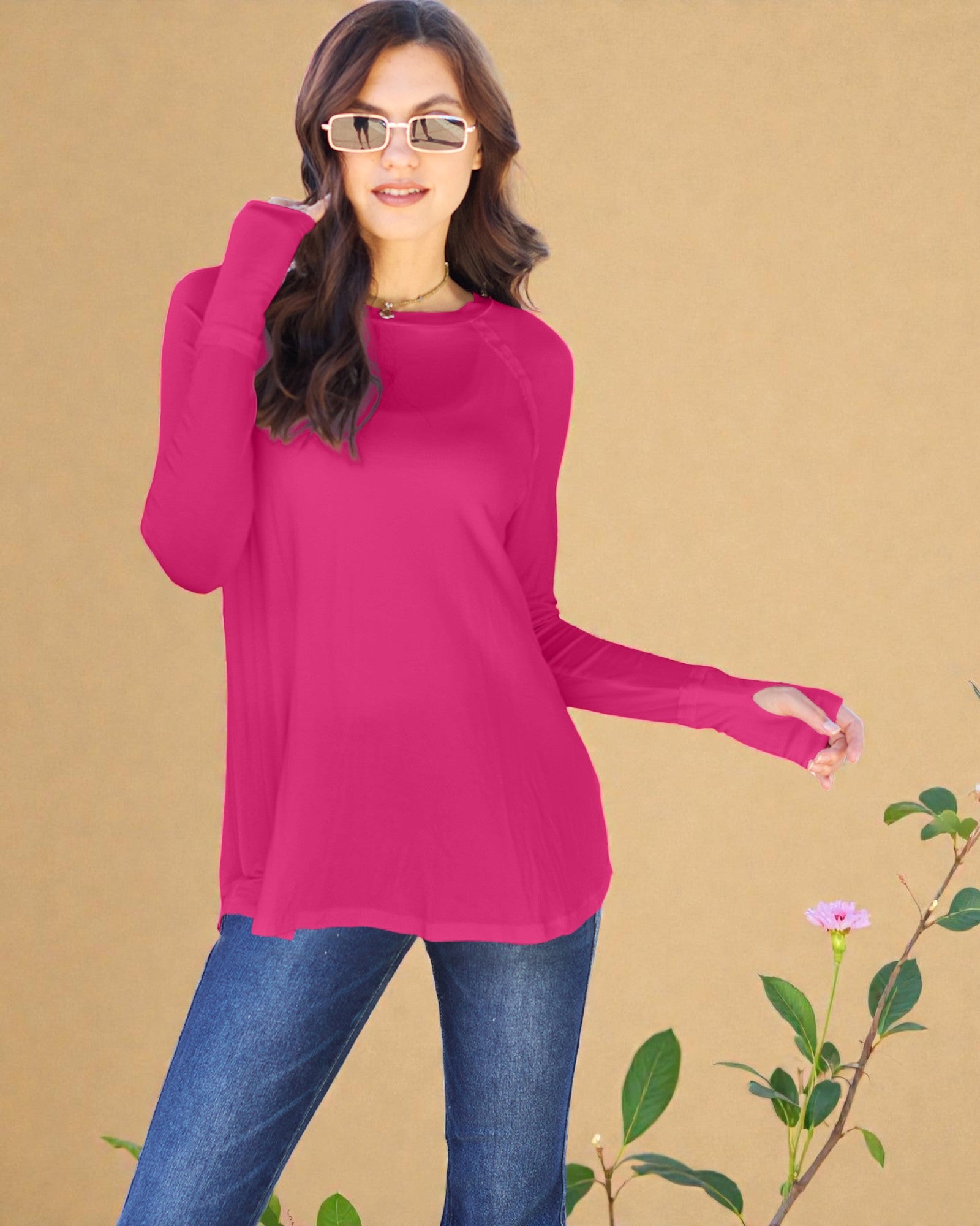 Woman wearing a bright pink long-sleeve top and blue jeans against a beige background