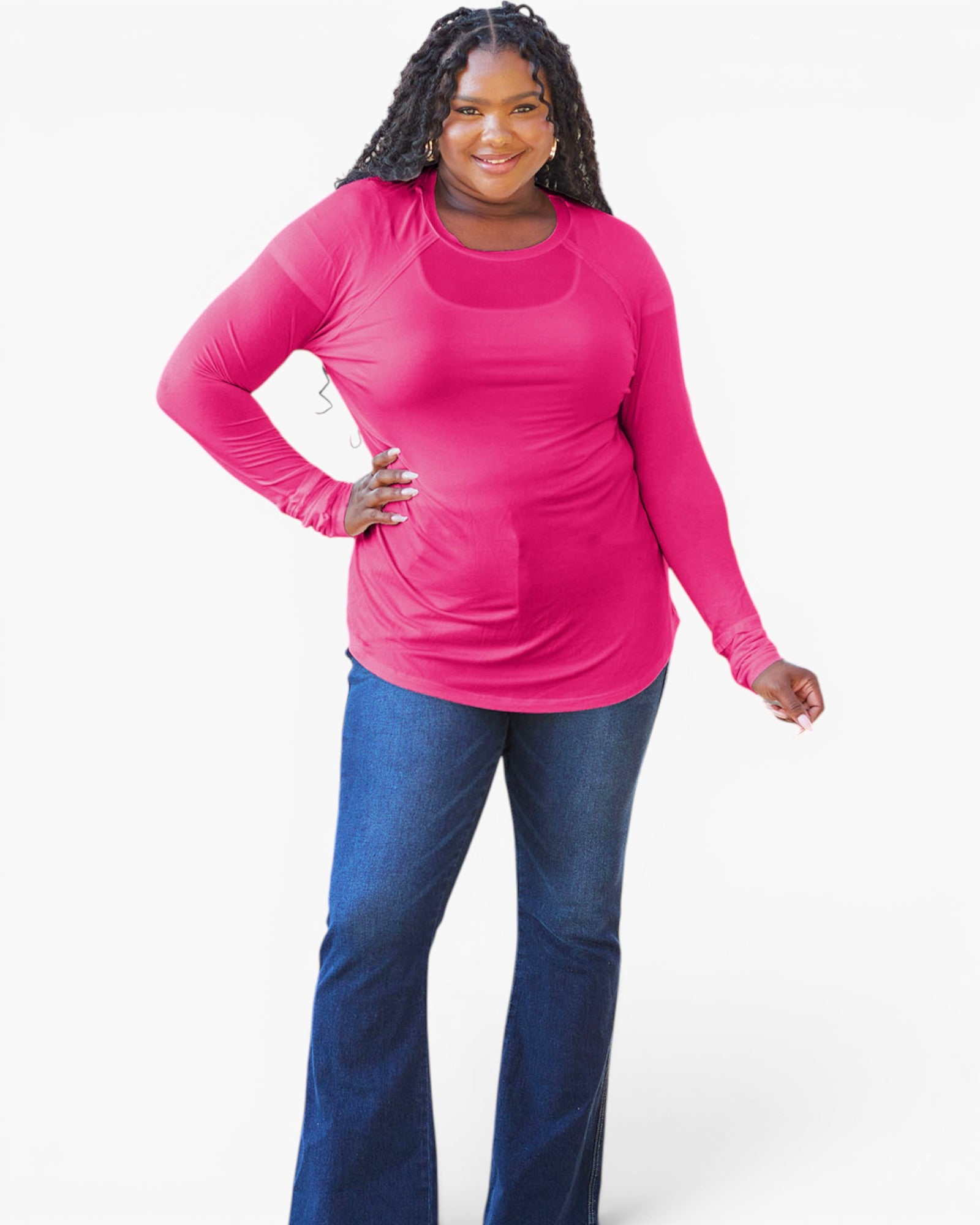 A woman modeling a bright pink long-sleeve athletic top with a scoop neckline and built-in sleeves, paired with blue jeans, against a light gray studio background.