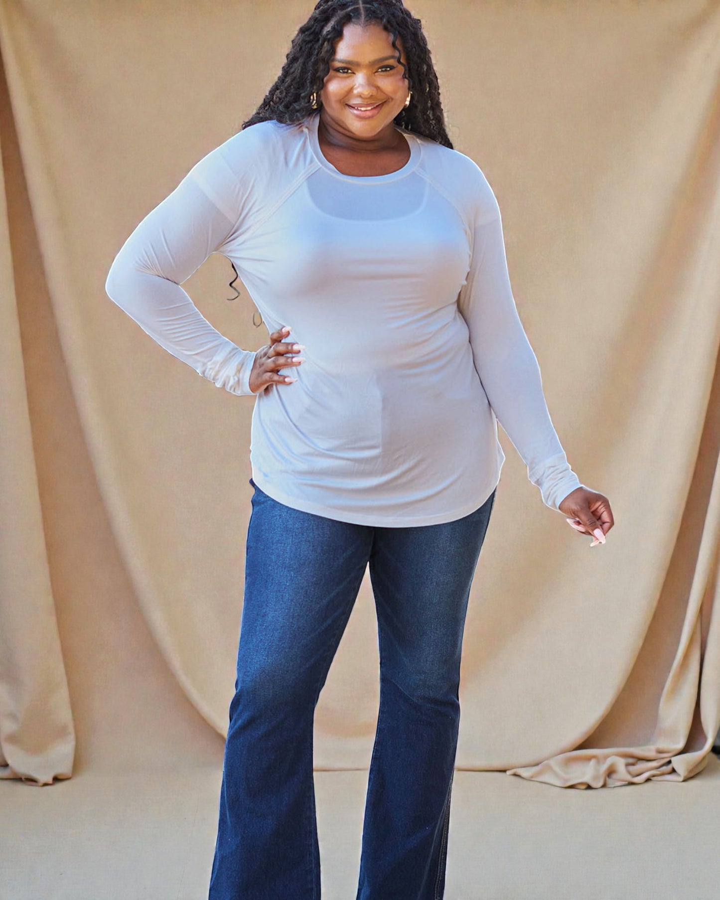 Woman wearing a white long-sleeve top and blue jeans against a beige background