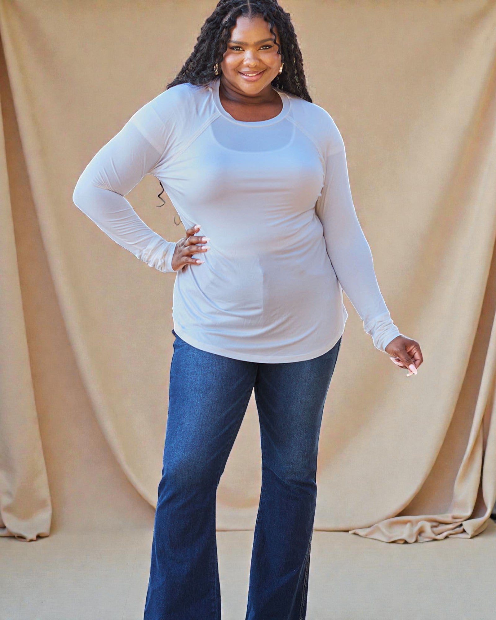 Woman wearing a white long-sleeve top and blue jeans against a beige background