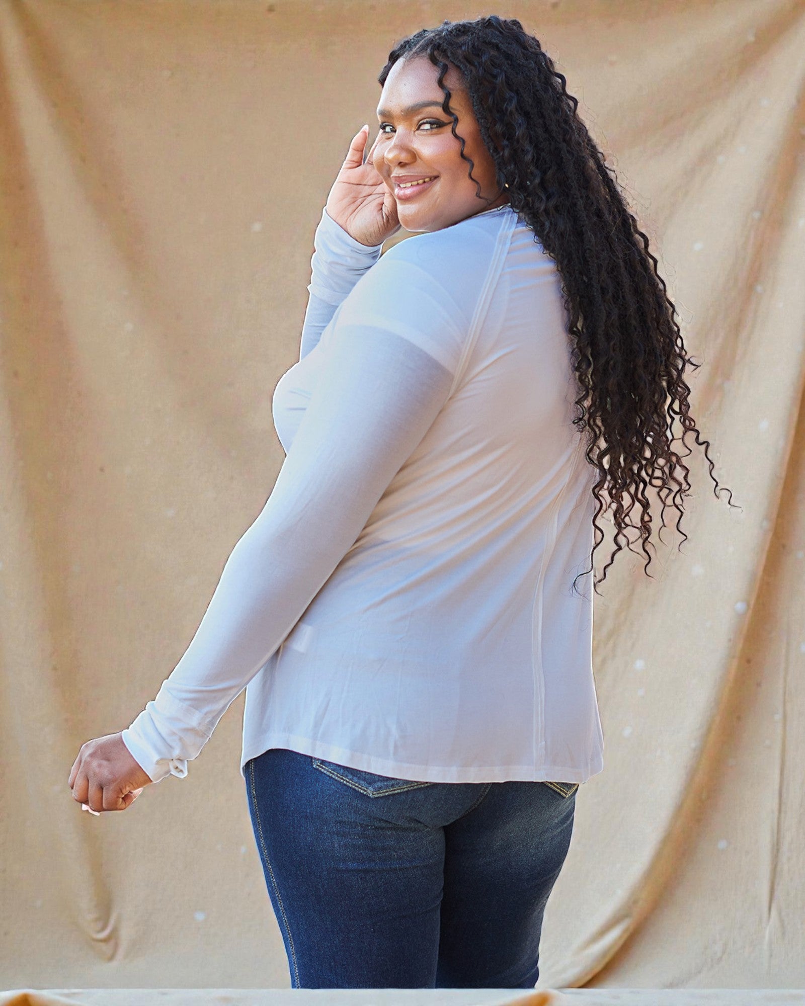 Woman wearing a light-colored long-sleeve top and dark jeans against a beige background