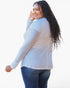 A woman with long, curly black hair is shown from a side-back angle wearing a light gray long-sleeve top and blue jeans against a plain white background.